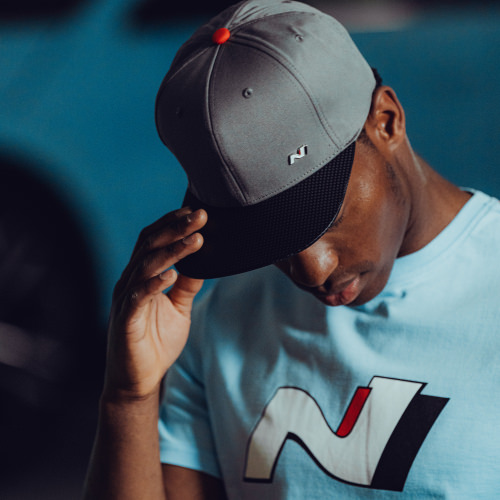 Man wearing a gray cap and light blue T-shirt with a stylized 'N' logo, tilting his head down.