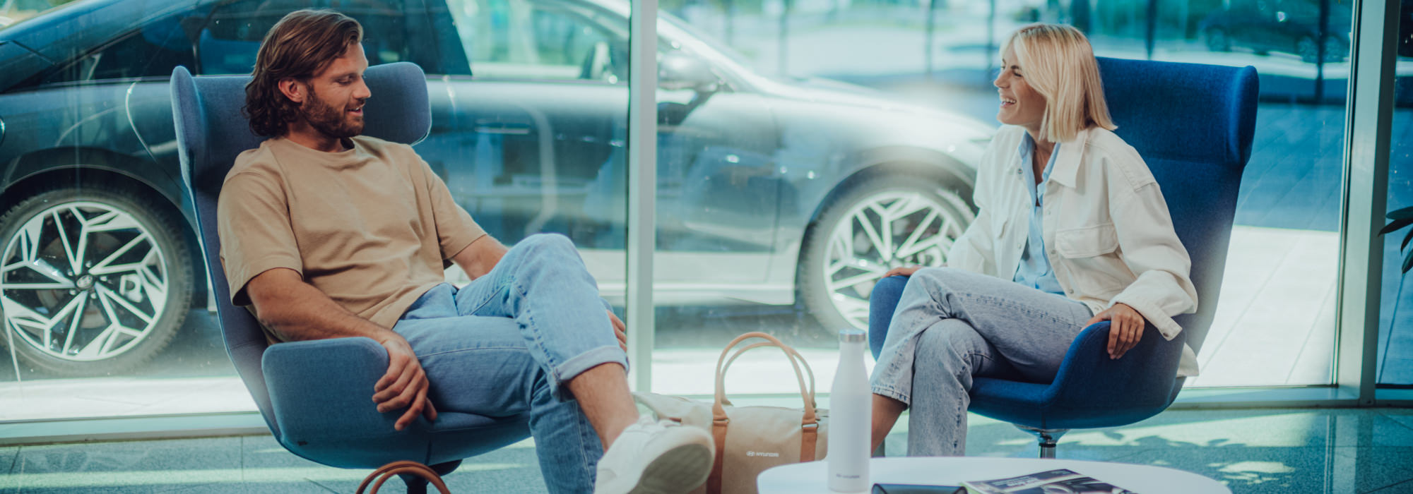Two people talking in a modern showroom lounge with a Hyundai car in the background.