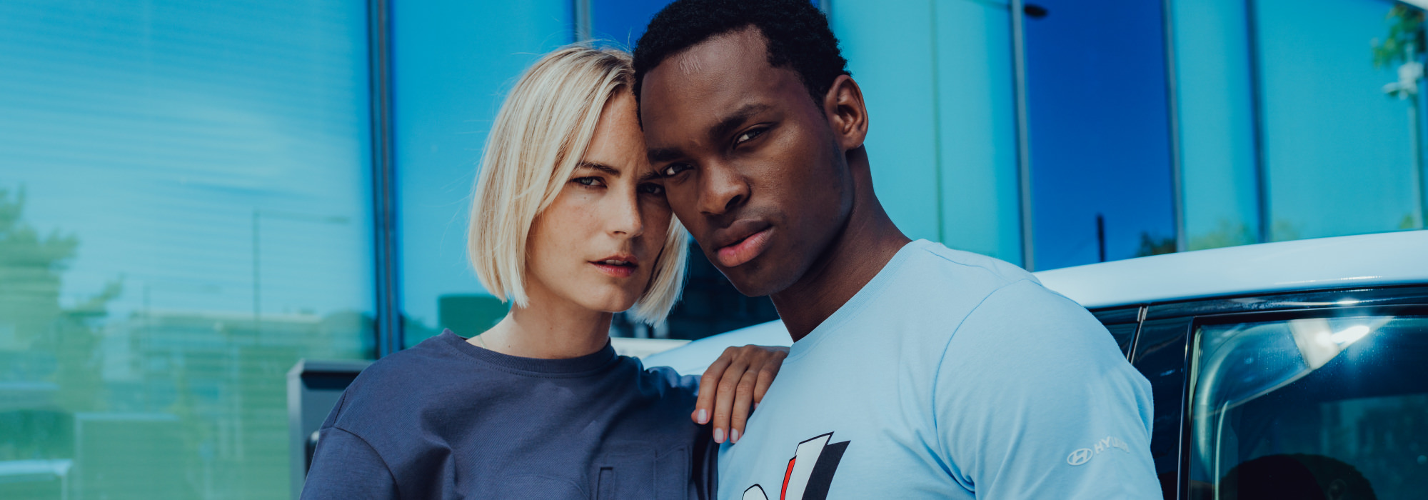 Two models in Hyundai N Collection apparel posing near a white car.